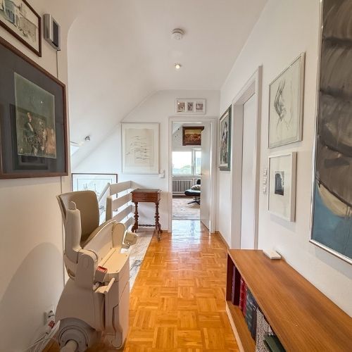 Heller Flur im Obergeschoss mit Parkettboden, Kunst an den Wänden und integriertem Treppenlift in einer Maisonette-Wohnung.